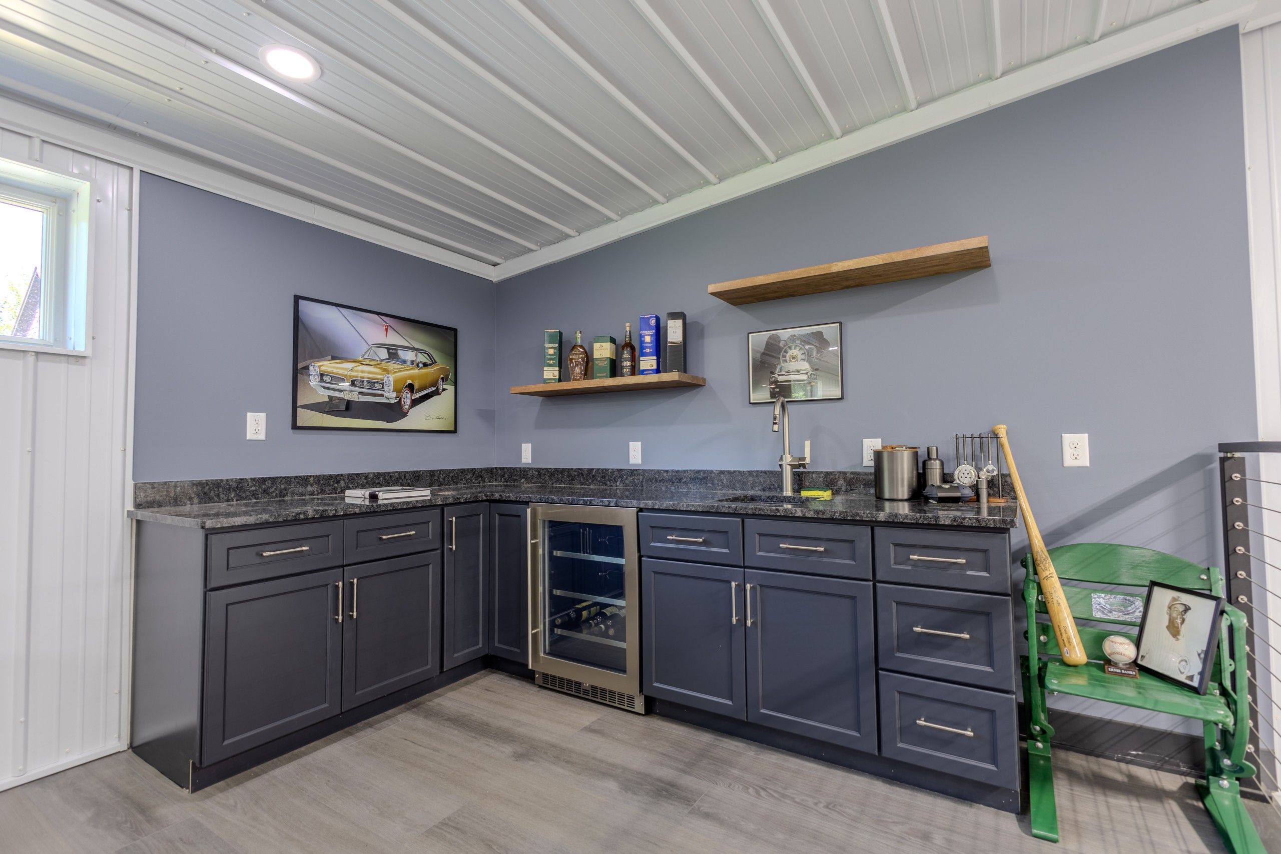 Custom mezzanine wet bar with dark cabinetry, countertop, sink and open shelving inside a luxury car collector garage in Wisconsin.