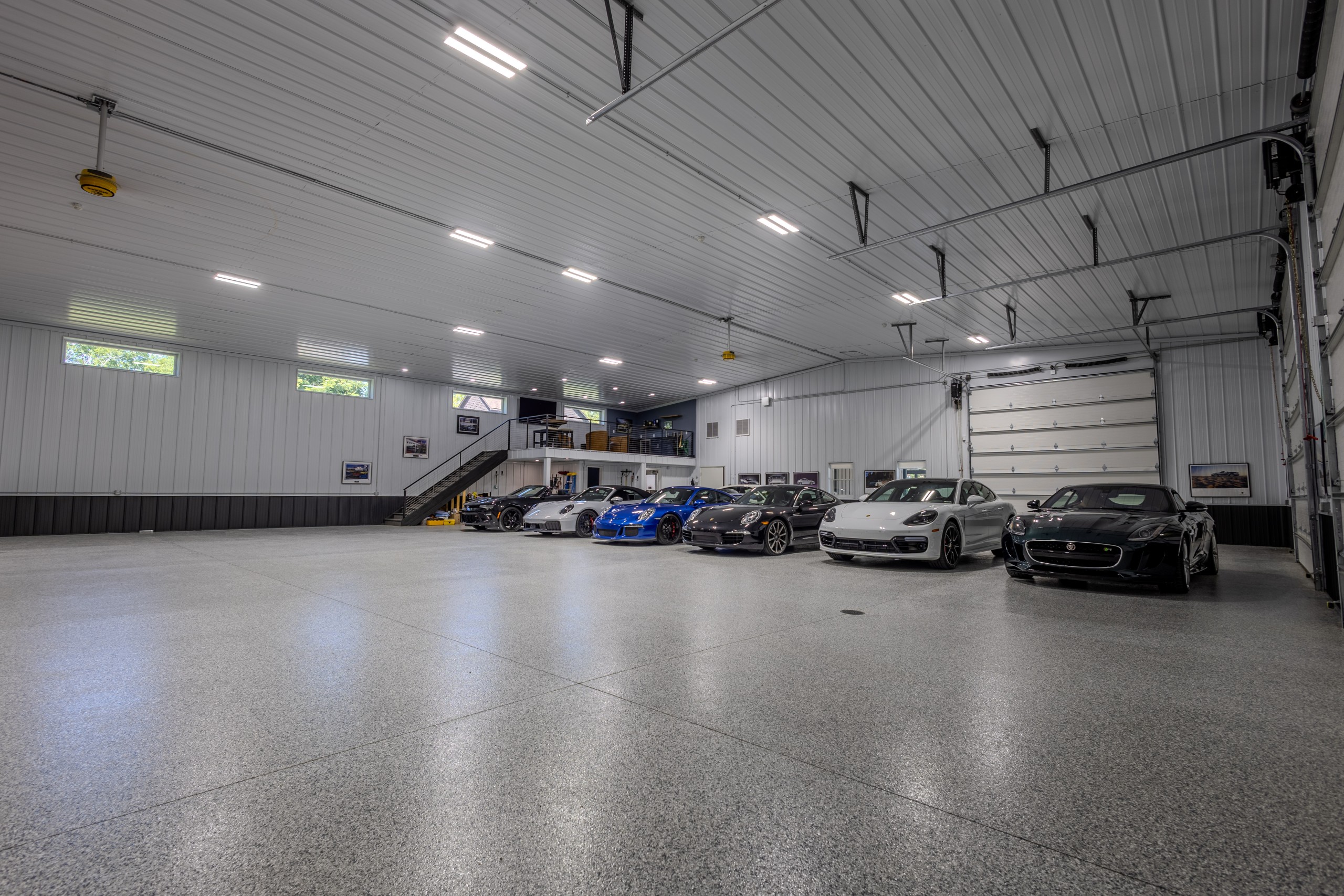 Spacious luxury car collector garage featuring engineered scissor trusses, a high interior ceiling, epoxy flooring and classic cars.