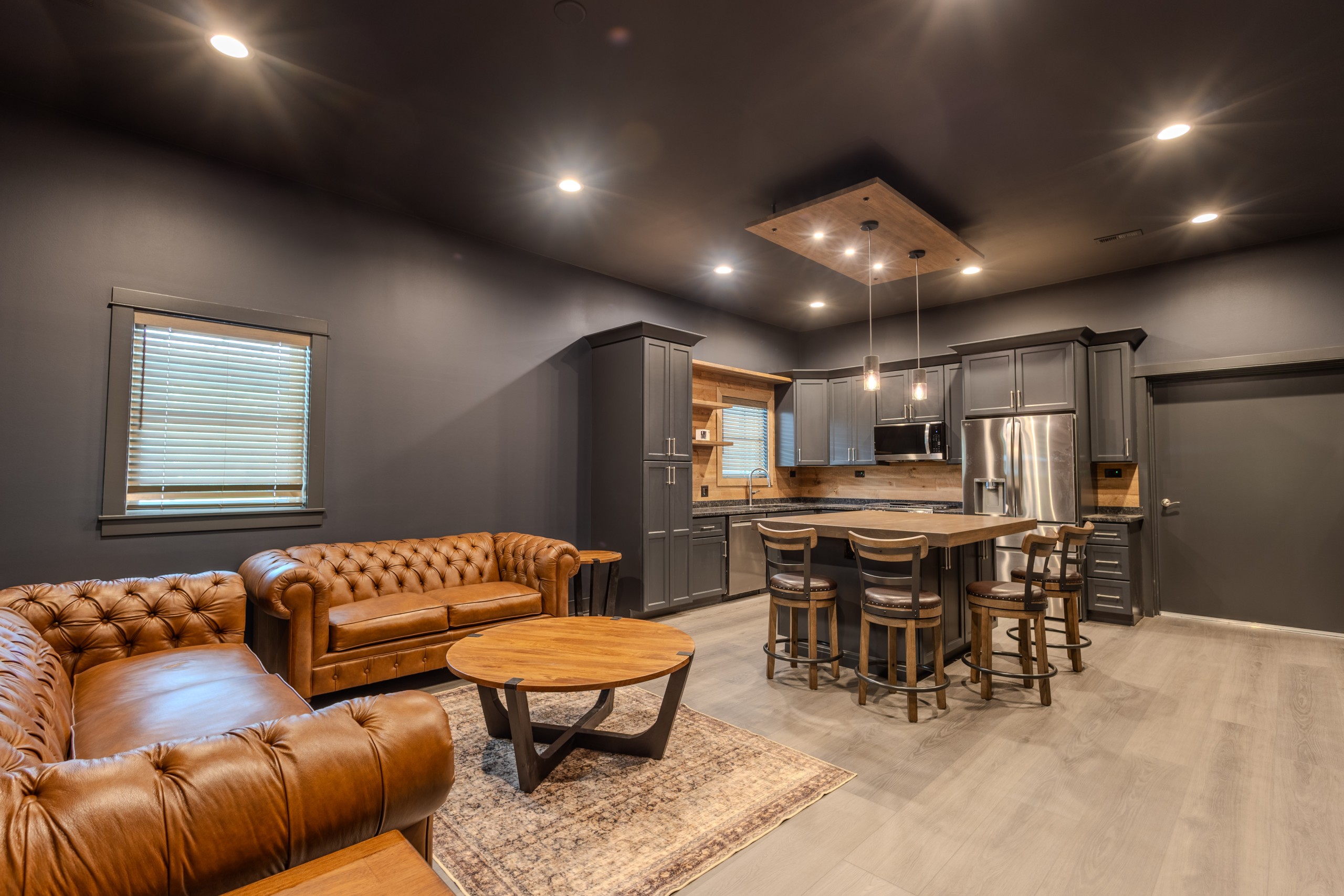 Private clubhouse lounge inside a luxury car collector garage featuring brown leather sofas, a wooden coffee table and modern interior finishes.