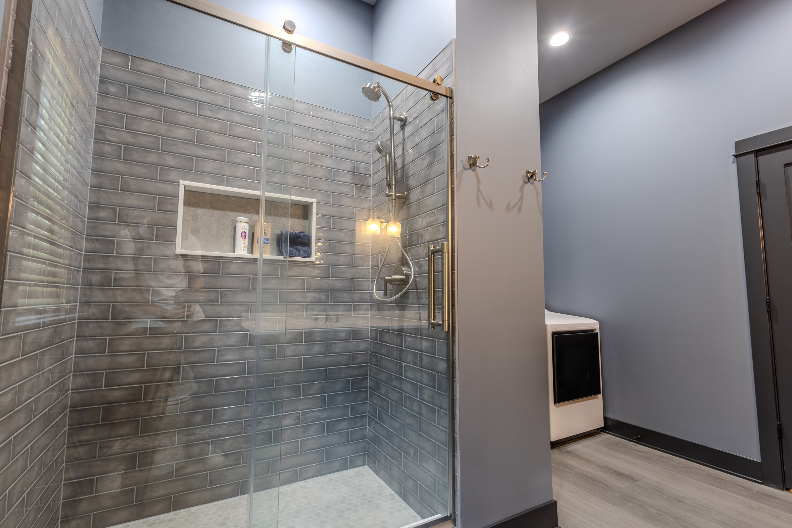 Custom tiled walk-in shower with glass enclosure and built-in wall niche inside a luxury car collector garage clubhouse in Delavan, Wisconsin.
