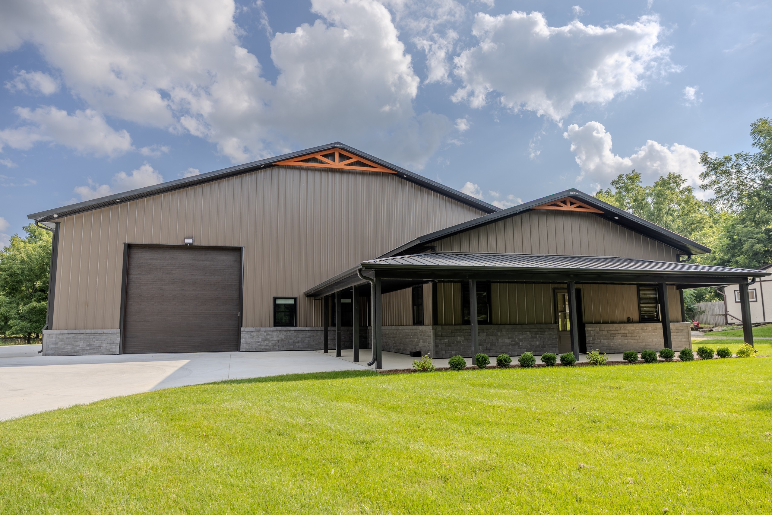 Wraparound covered porch on a luxury car collector garage and private clubhouse in Delavan, Wisconsin, featuring dark steel roofing and decorative cedar trusses.